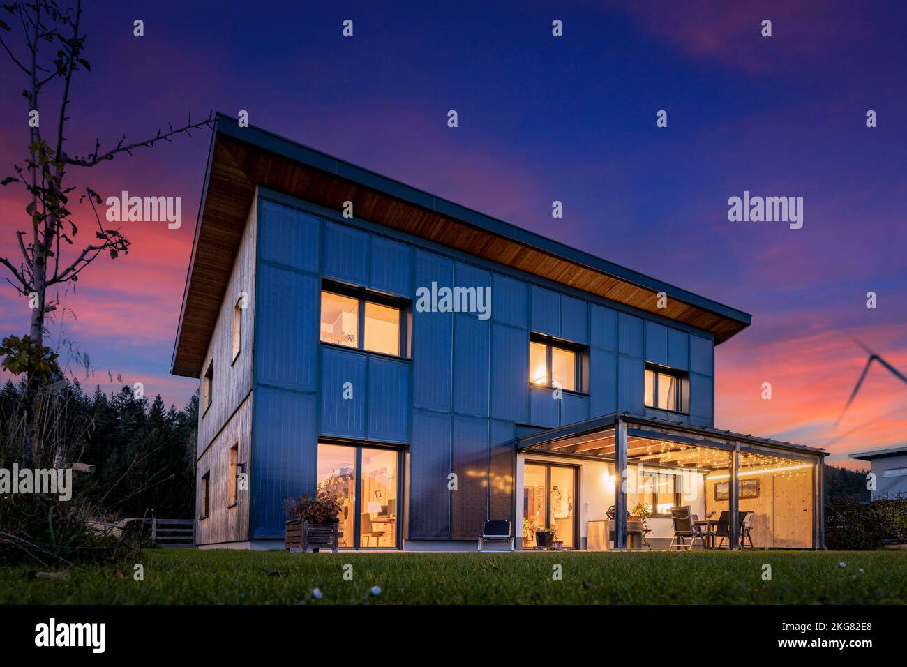 Illuminated wooden prefabricated house in the evening with a sustainable and self-sufficient energy concept with photovoltaic and solar thermal collec Stock Photo