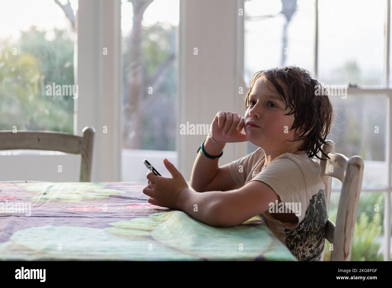 Boy (8-9) sitting at a table and using smart phone Stock Photo