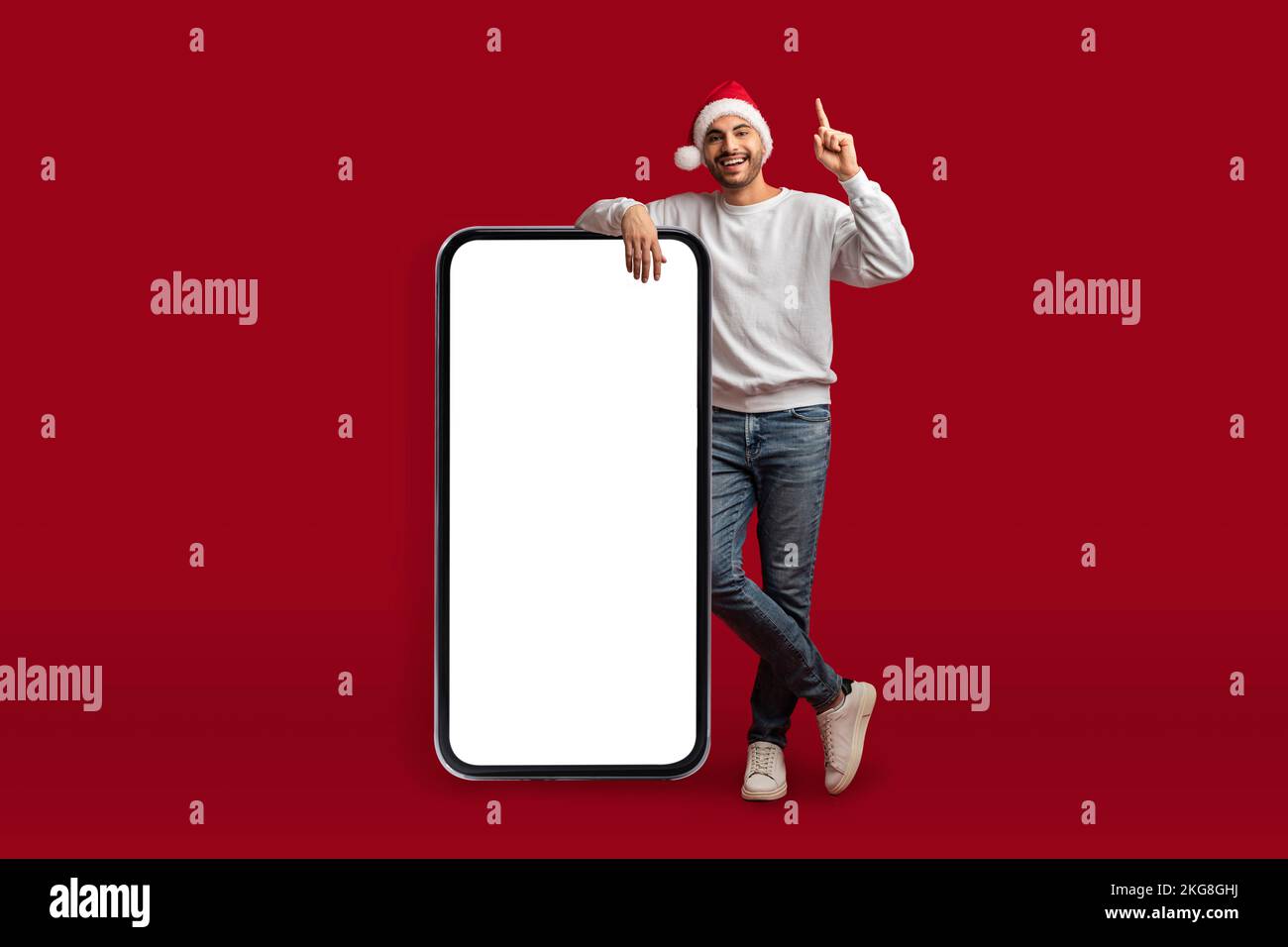Chistmas Idea. Excited Arab Man In Santa Hat Standing Near Blank Smartphone Stock Photo