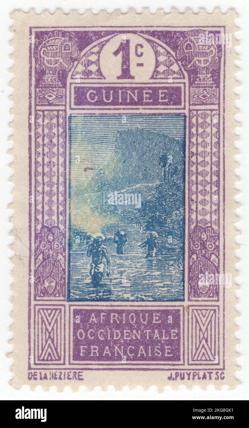 FRENCH GUINEA - 1913: An 1 centime violet and blue postage stamp depicting scene Ford at Kitim. Several people overcome a water obstacle, carrying a load on themselves. Around the jungle, behind a big mountain Stock Photo