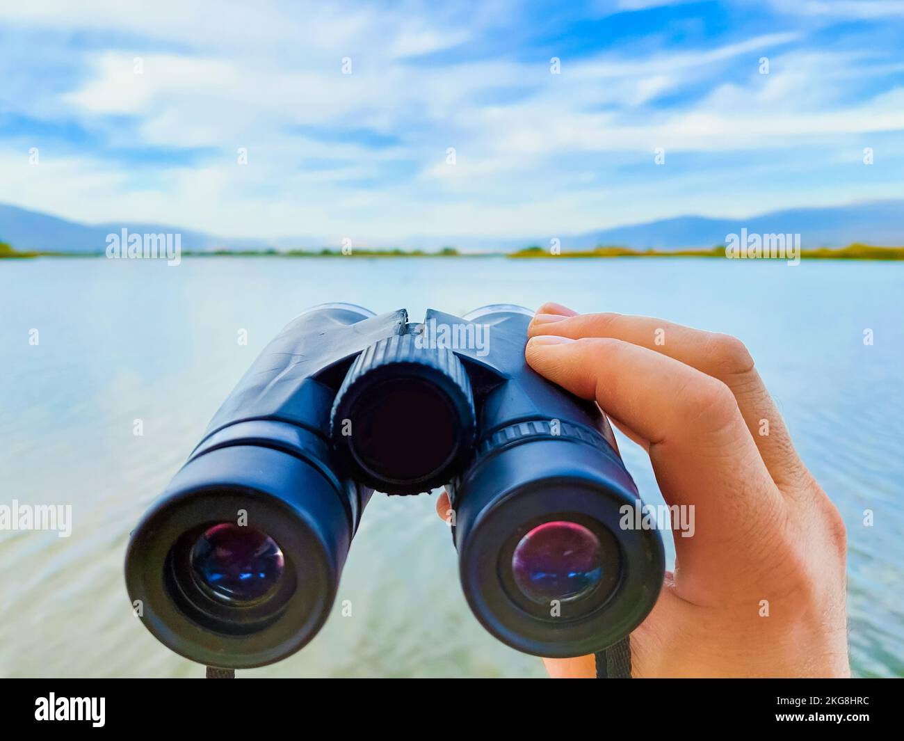 Hands holding binoculars to watch migrating birds over Lake Hula in Israel Stock Photo