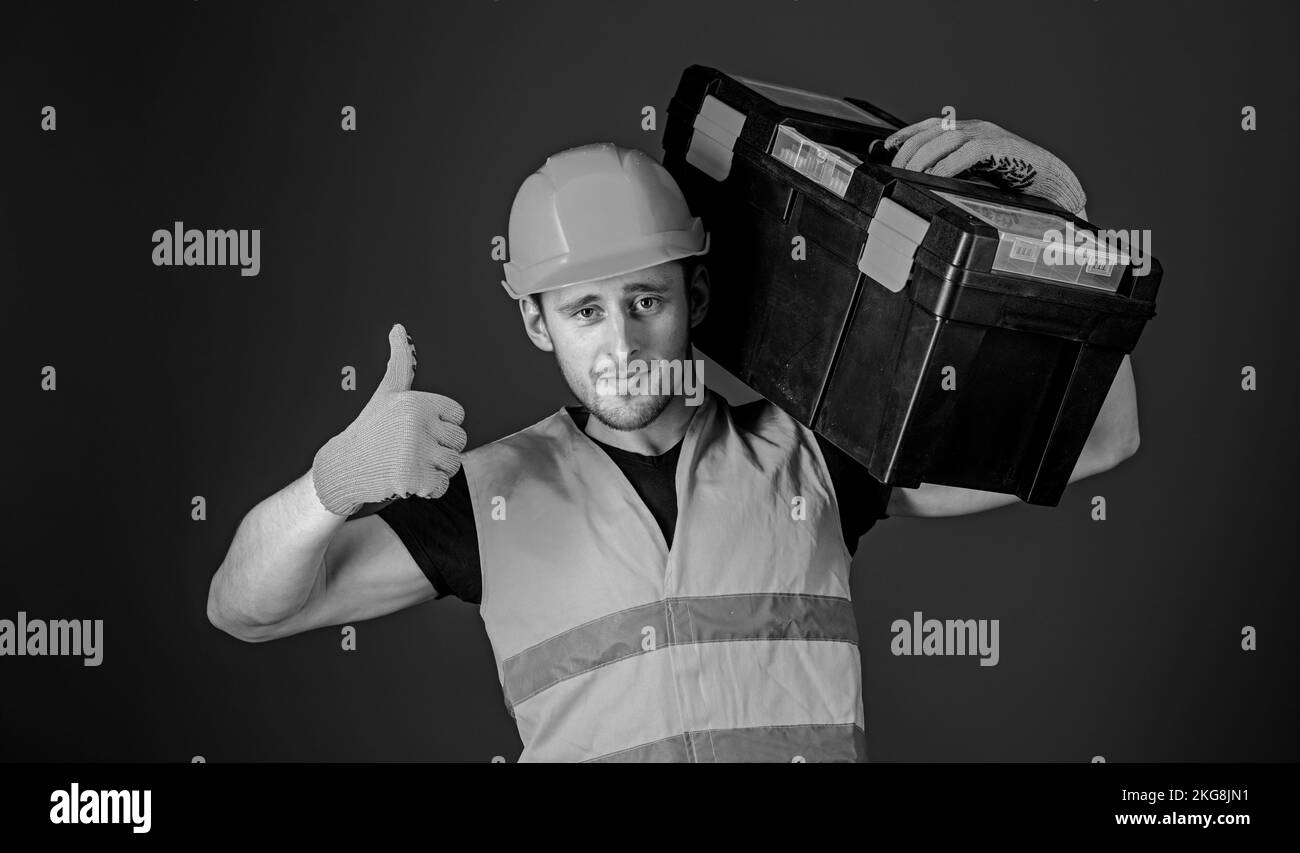 Man in helmet, hard hat holds toolbox and shows thumb up gesture, blue