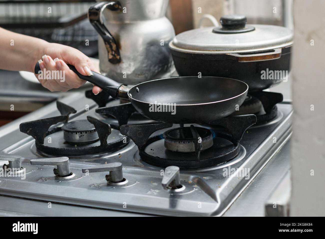 woman's hand placing a small frying pan on the burner of a gas stove to fry an egg. Stock Photo