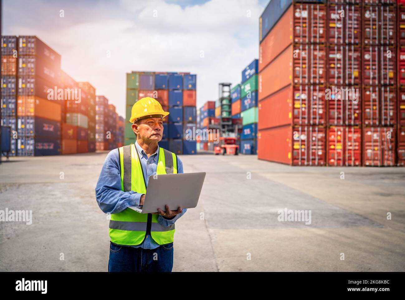 Engineer or foreman holding laptop and wears PPE checking container