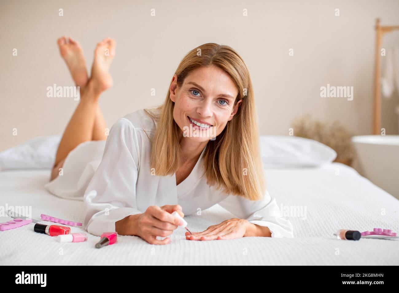 Attractive middle aged lady in solky bathrobe lying on bed and making ...