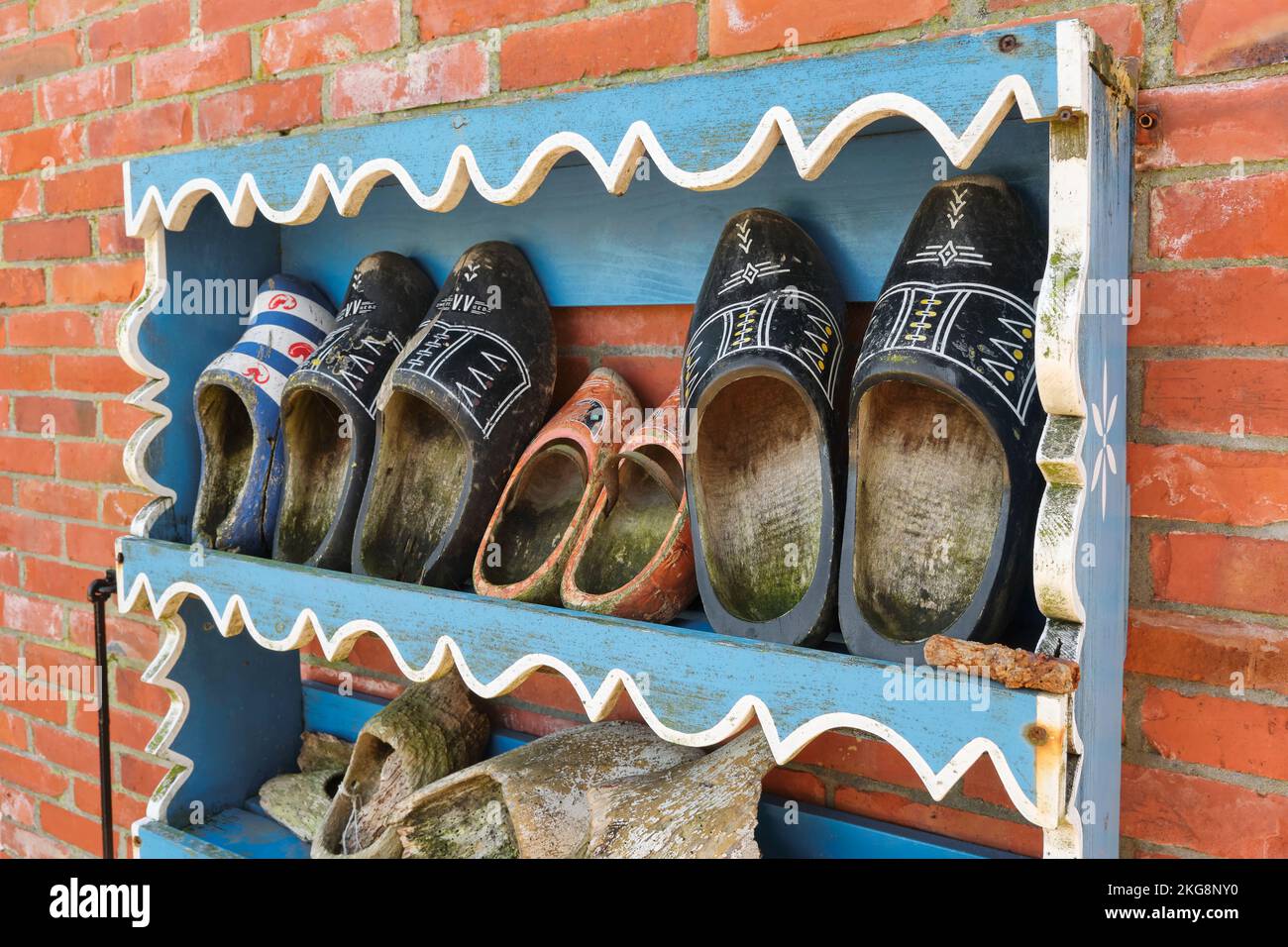 Old worn-out Dutch clogs or wooden shoes in a rack on a red brick wall Stock Photo