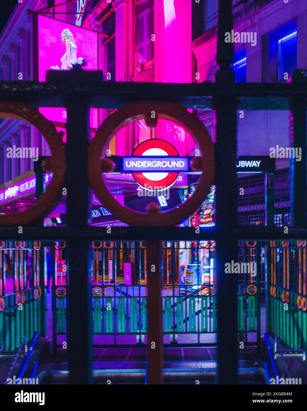 A London underground limited roundel at Tottenham court road, London, framed by railings which are above the station entrance at night. Stock Photo