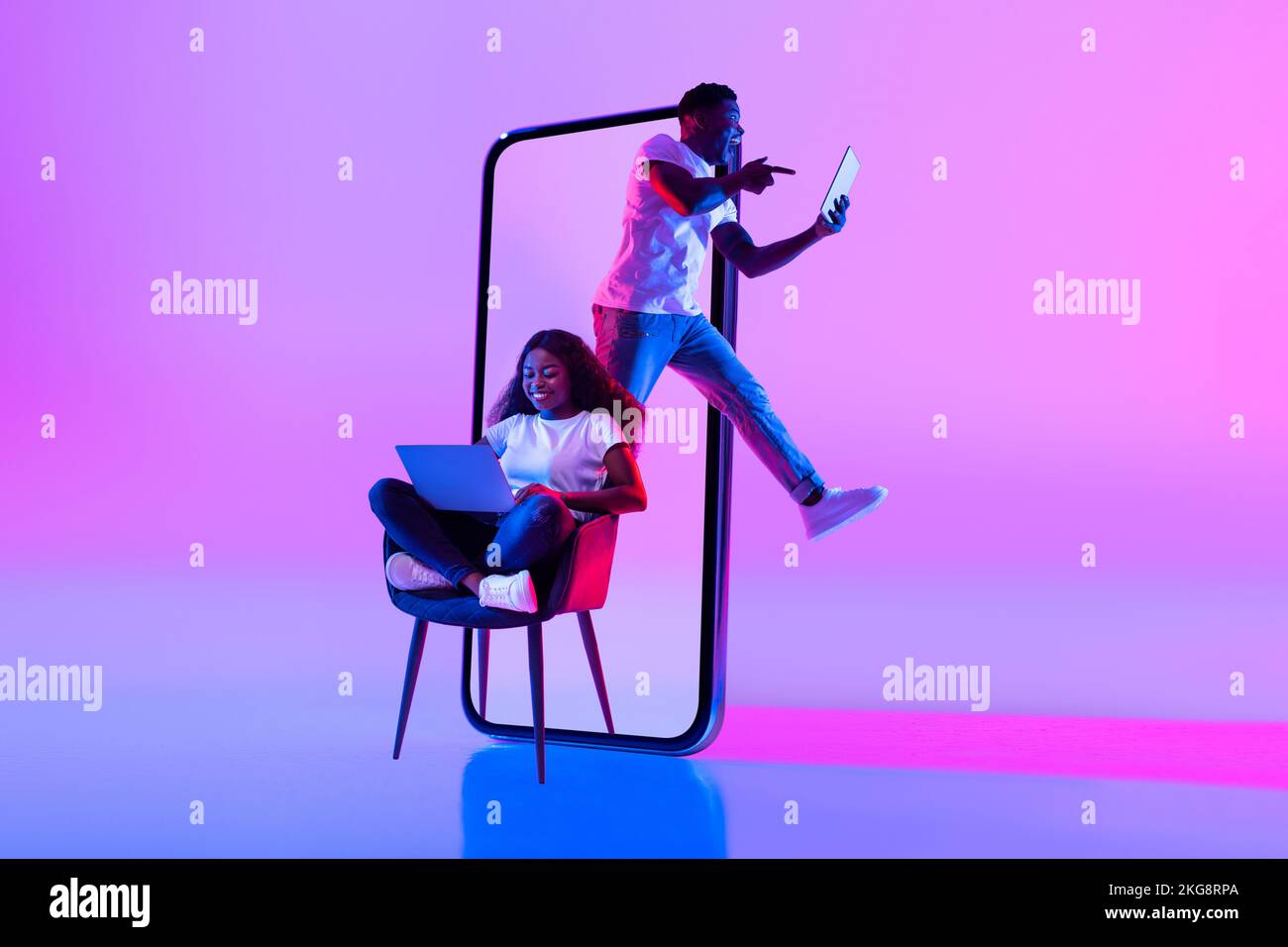 Smiling excited young black man jumping with tablet near huge phone ...