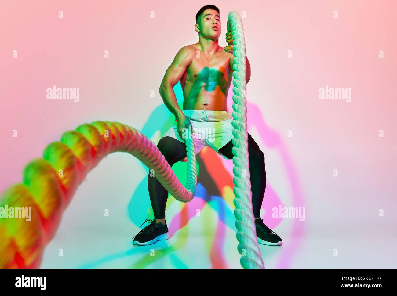 Portrait of young muscular man training, pulling rope isolated over ...