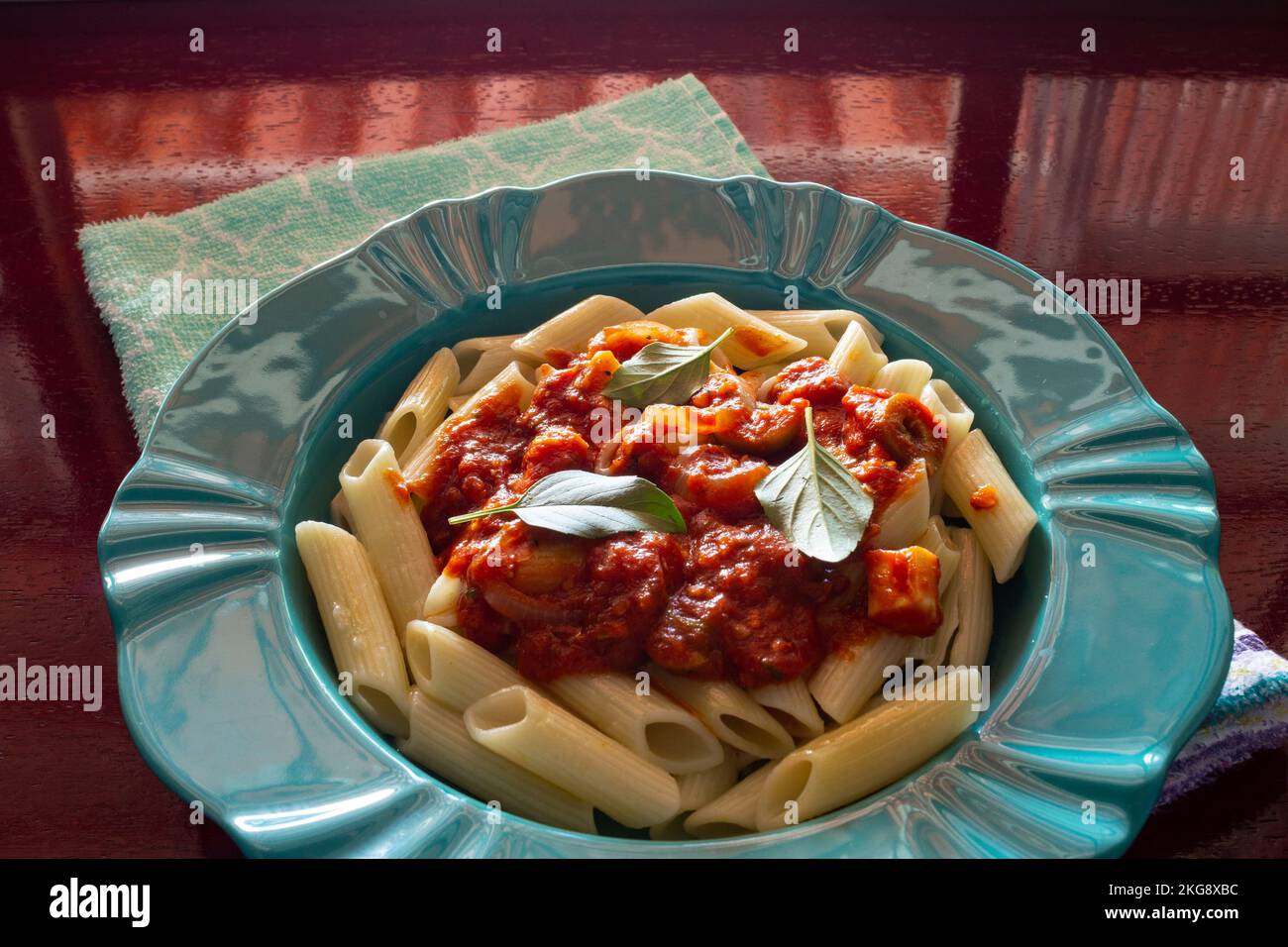 Goiânia, Goias, Brazil – November 22, 2022: A bright green plate with a portion of pasta (penne) with tomato sauce and basil leaves. Stock Photo