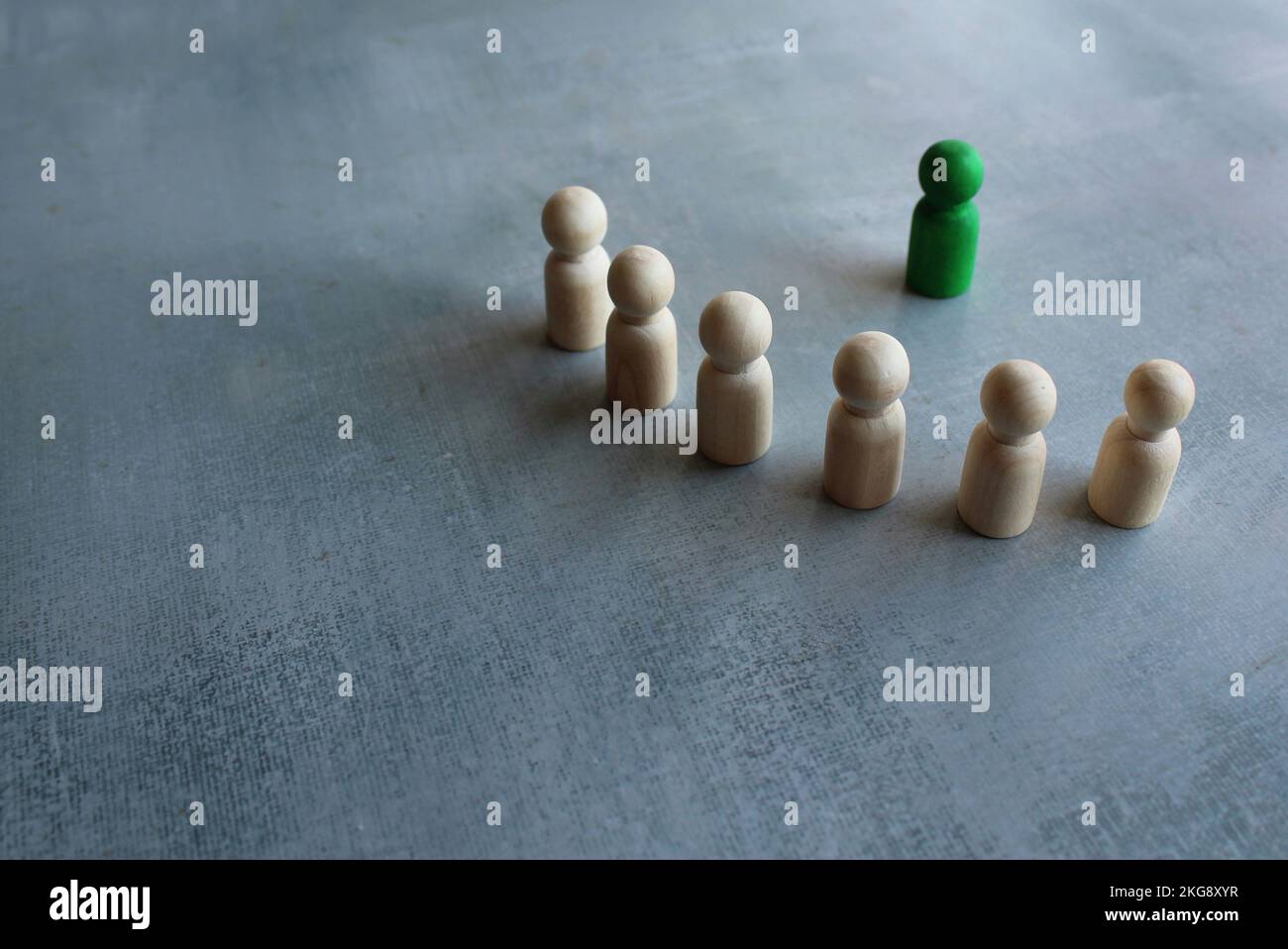 Green wooden doll in front of white wooden dolls. Leader, coaching and mentoring concept. Stock Photo