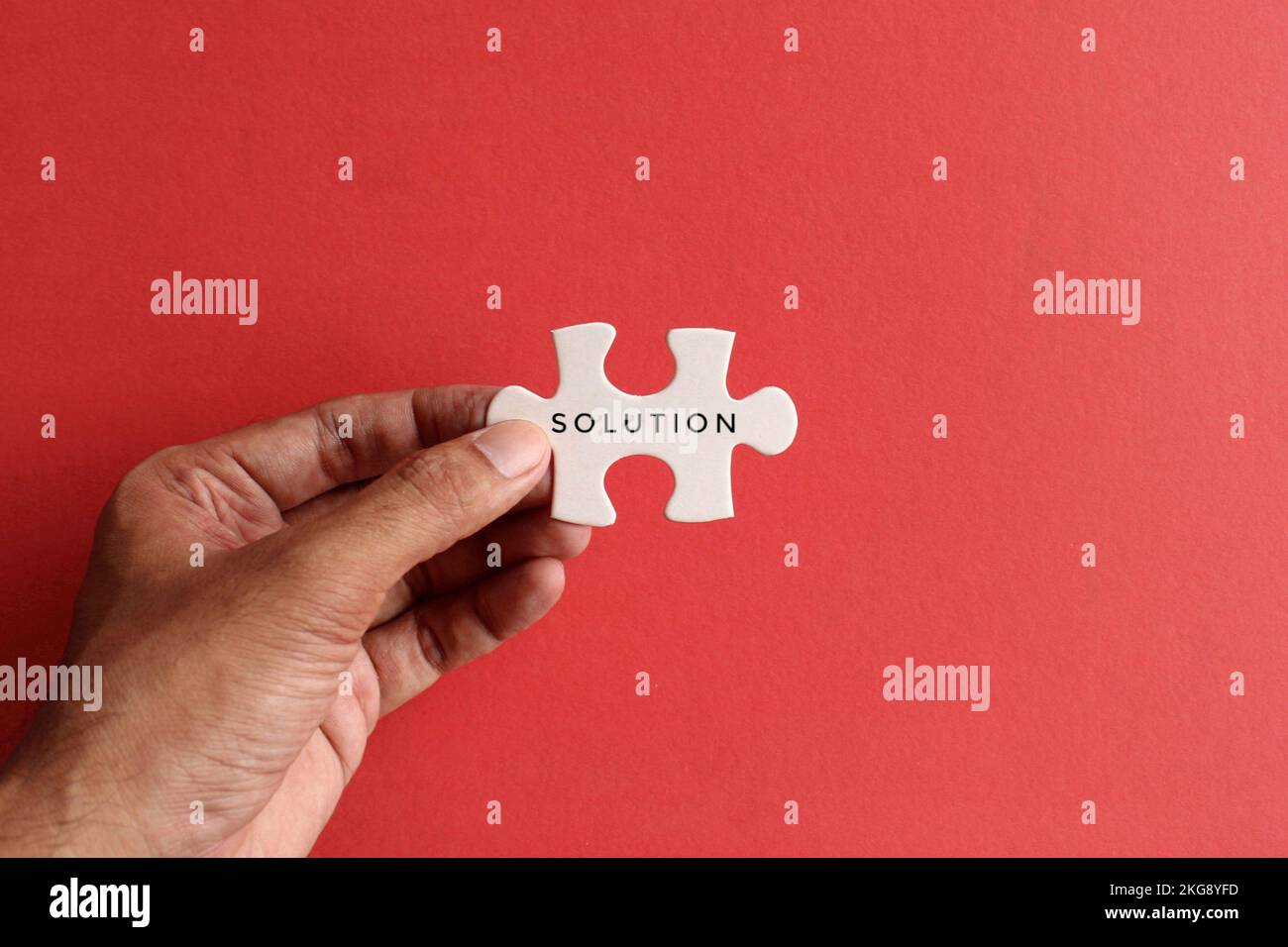 Hand holding puzzle pieces with text SOLUTION on red background. Top view with copy space Stock Photo