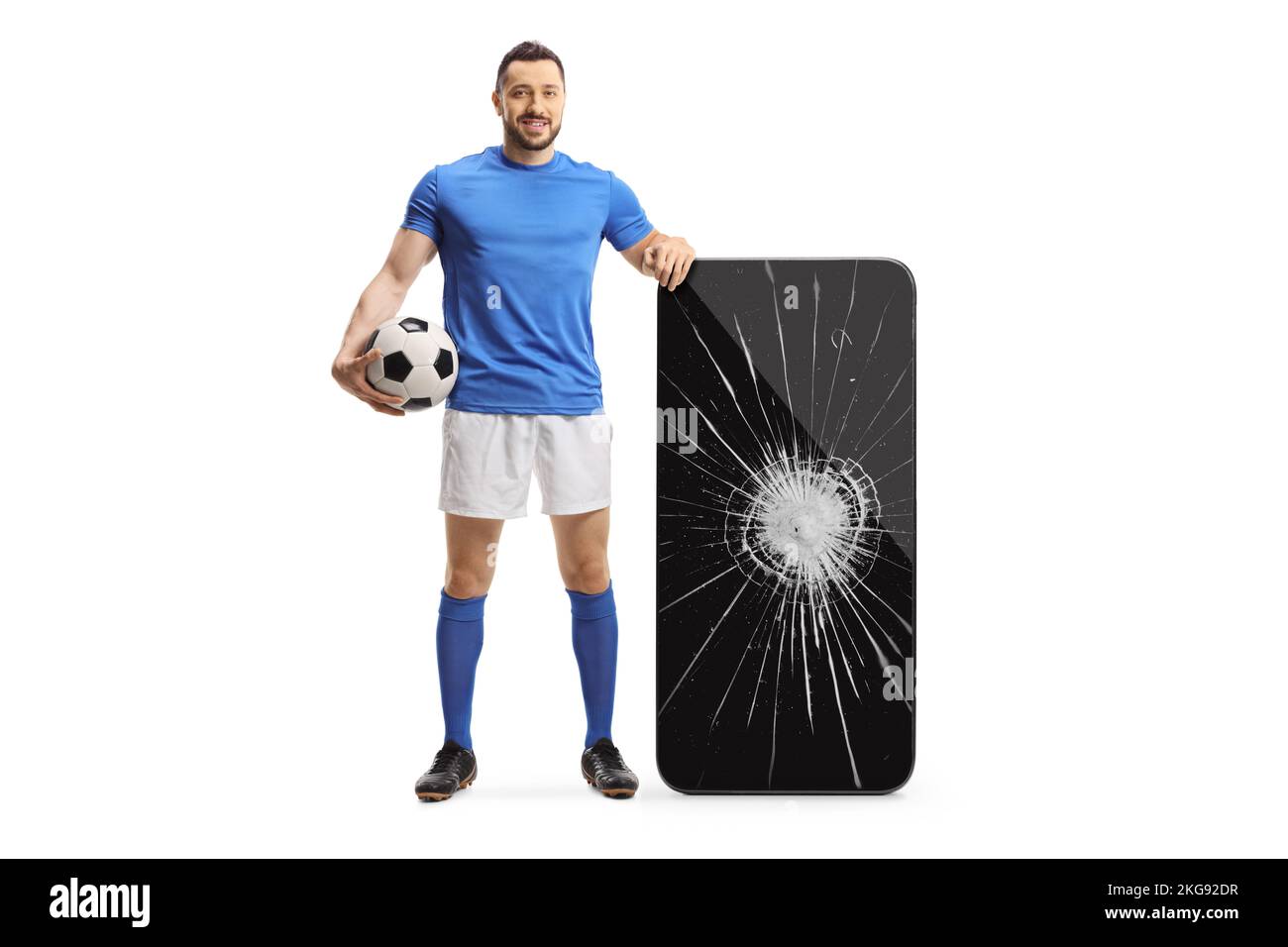 Full length portrait of a football player standing next to a big smartphone with broken screen isolated on white background Stock Photo