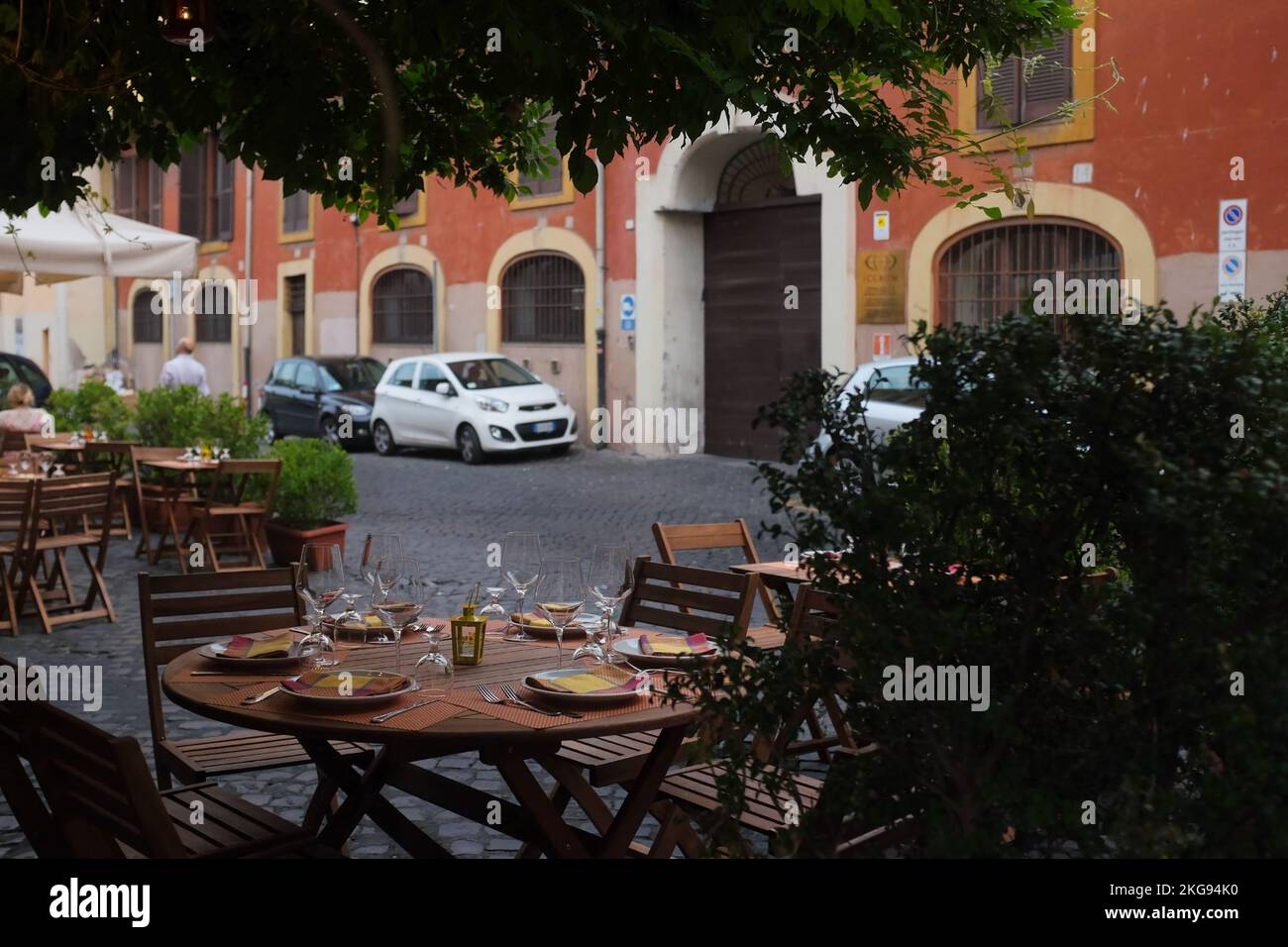 Cozy outdoor cafe table setting in the charming neighborhood of Trastevere. Al fresco restaurant dining setup along a cobblestone street in Rome, Italy. Stock Photo