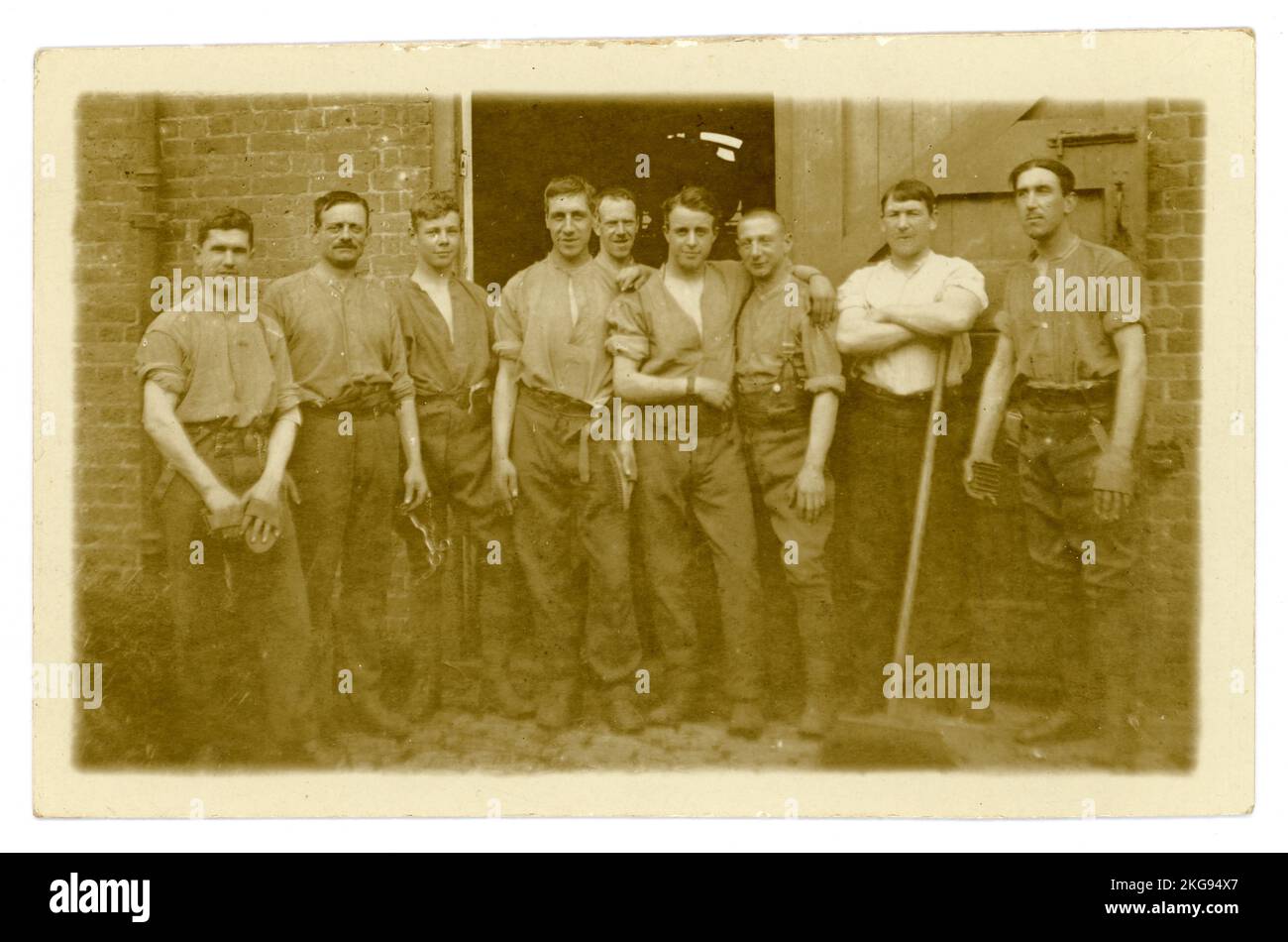 Original WW1 era postcard of cavalrymen of the 11th Hussars, (Prince Albert's Own also  known as the Cherry Pickers) posing for a relaxed, informal group photograph, in shirt sleeves, outside the stables after grooming their horses at Aldershot military training camp. The young man on very far LH of the group is Arthur Darling from Norwich, Norfolk. This was taken just before they were due to be transferred elsewhere, (possibly to York) later they may have been sent to join the battle at Messines) as infantry, not the cavalry. Location: Aldershot, Hampshire, England, UK. Circa October 1914. Stock Photo