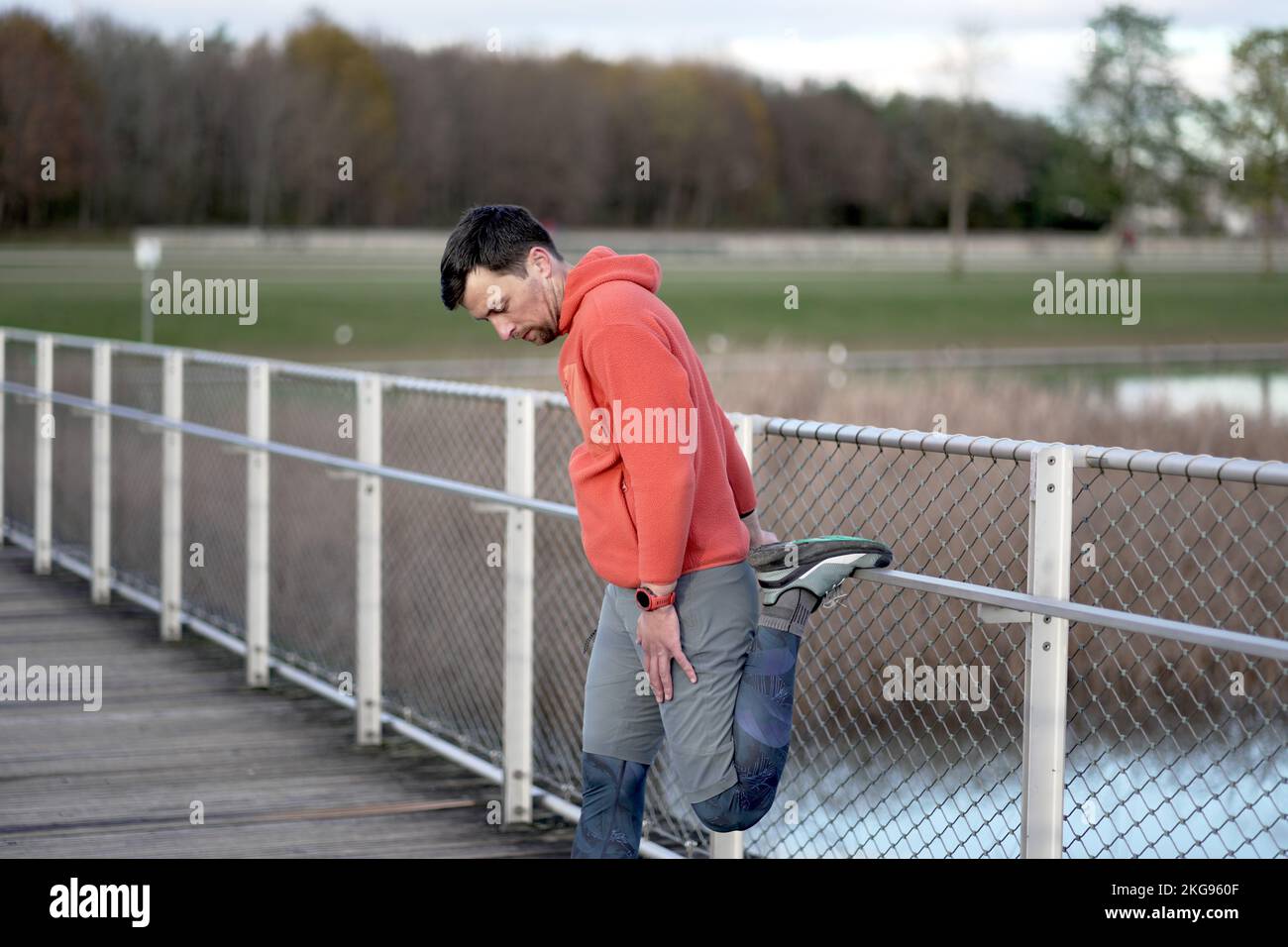 Athlete warming up before an outdoor cardio workout. A jogger warms up his muscles for a jog in nature on a wooden bridge in the cold fall weather Stock Photo