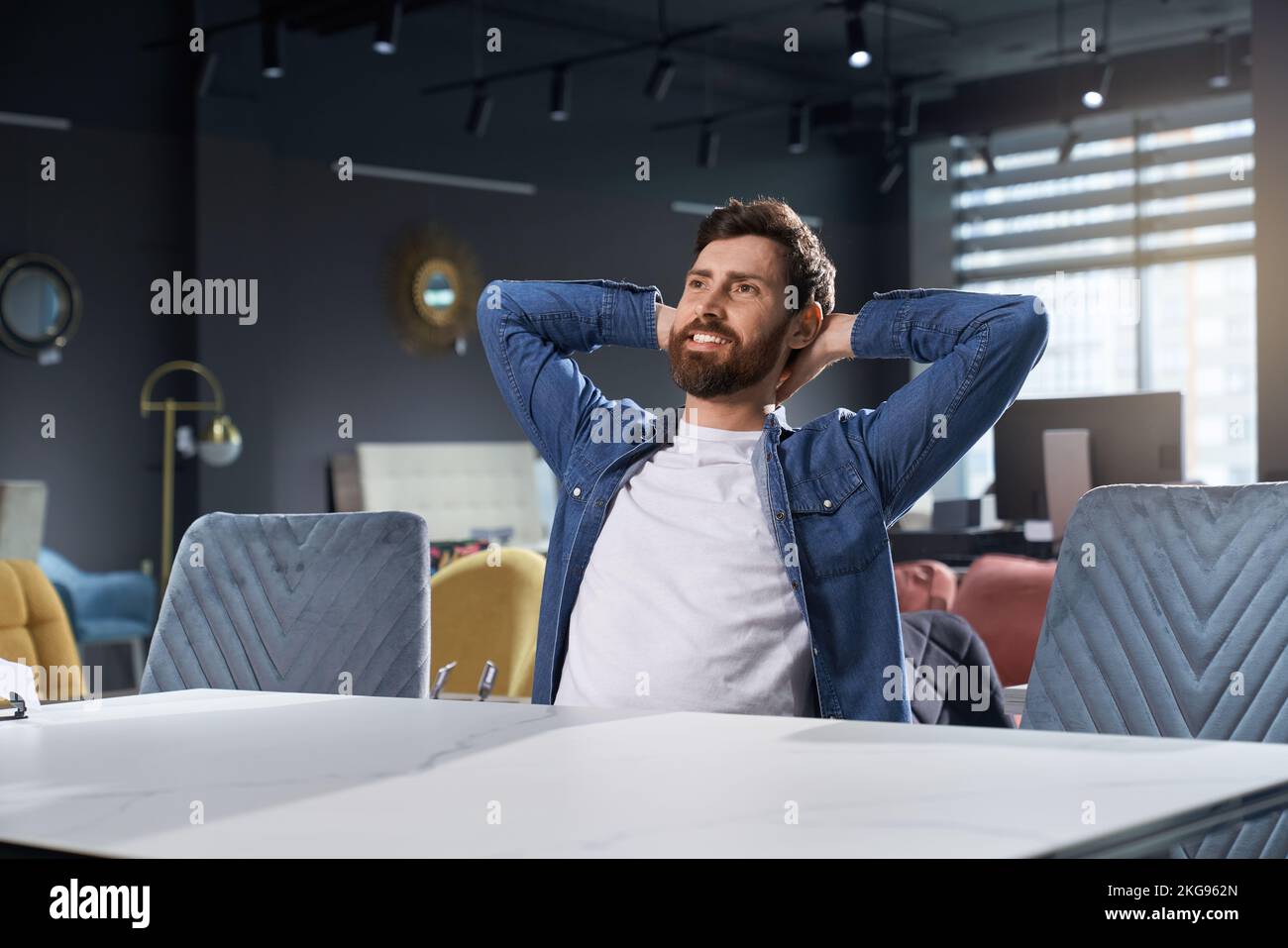 Happy, relaxed caucasian man sitting on new cozy chair in furniture shop. Portrait of cheerful bearded guy dreaming, feeling pleased and satisfied, wh Stock Photo