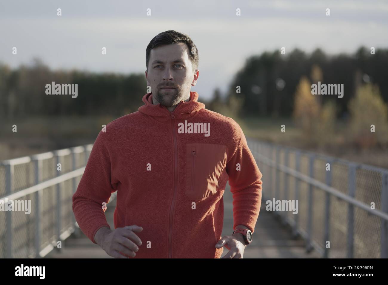 Male in orange hoodie running through national park across wooden bridge in wilderness in the cold fall weather. Sportsman does a fitness workout Stock Photo
