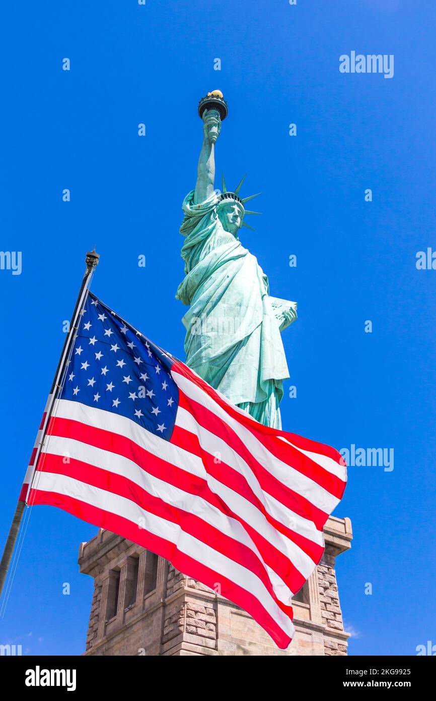American flag on flagpole waving in the wind against a blue sky with Statue of Liberty Stock Photo