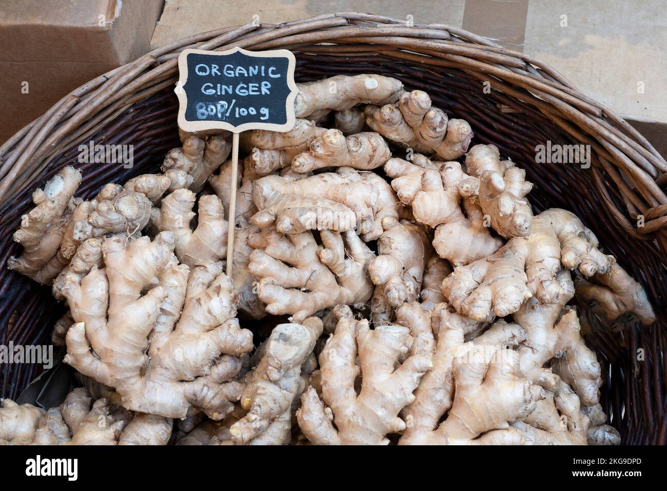 Fresh organic ginger, Zingiber officinale, for sale in on a fresh food market stall.The ginger root is displayed in a basket with a price tag per 100g Stock Photo