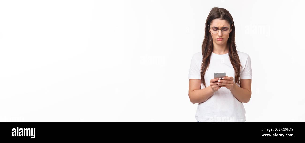 Communication, technology and lifestyle concept. Portrait of troubled and confused young woman reading strange message, frowning as looking mobile Stock Photo