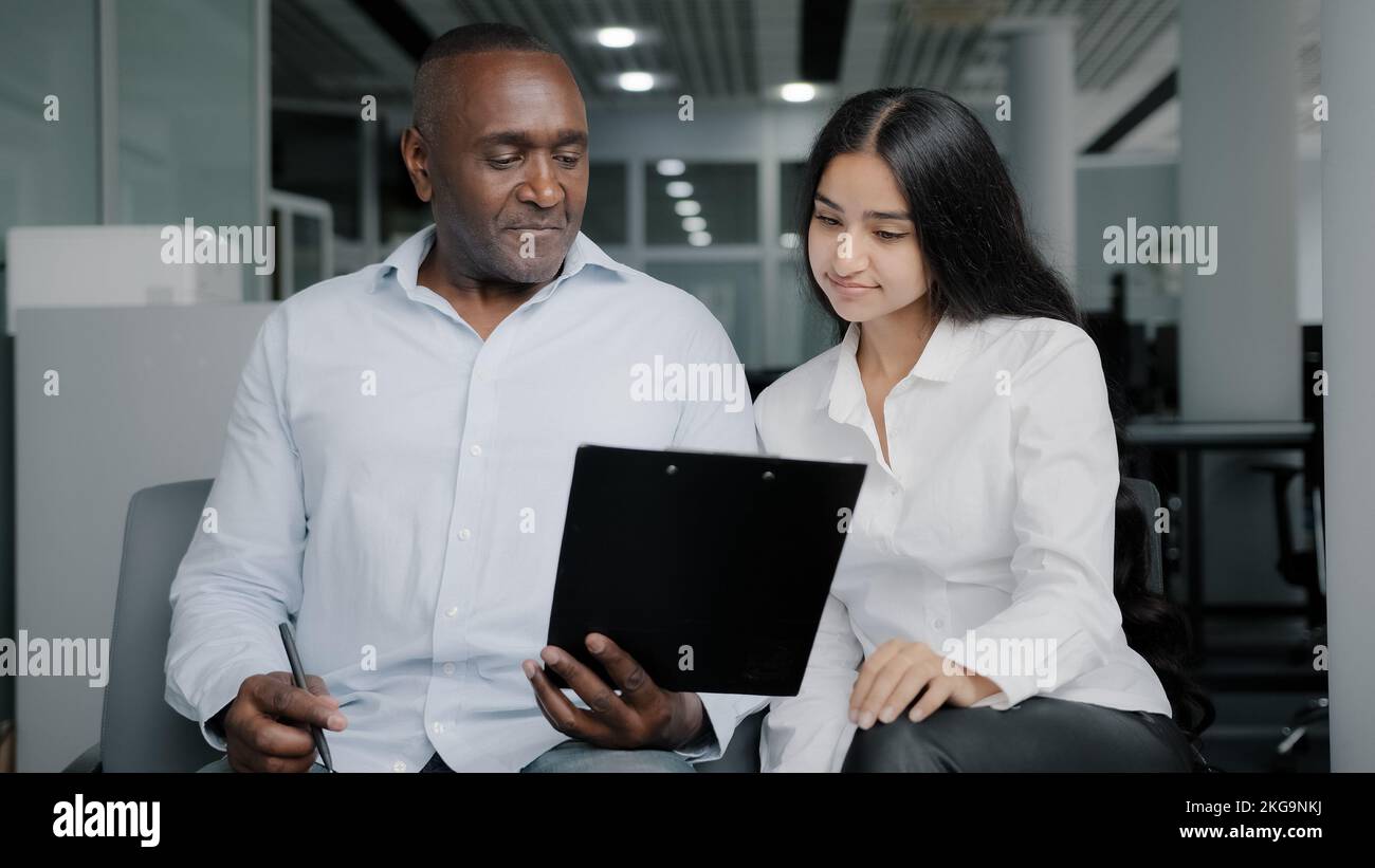 Diverse business partners sit in office discuss paper instruction african businessman show documentation in folder tablet to arabian female colleague Stock Photo