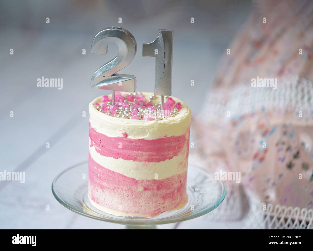 21st Birthday cake pink and silver cake with some sprinkles and 21st candlelight with a woman dress at the background. Stock Photo