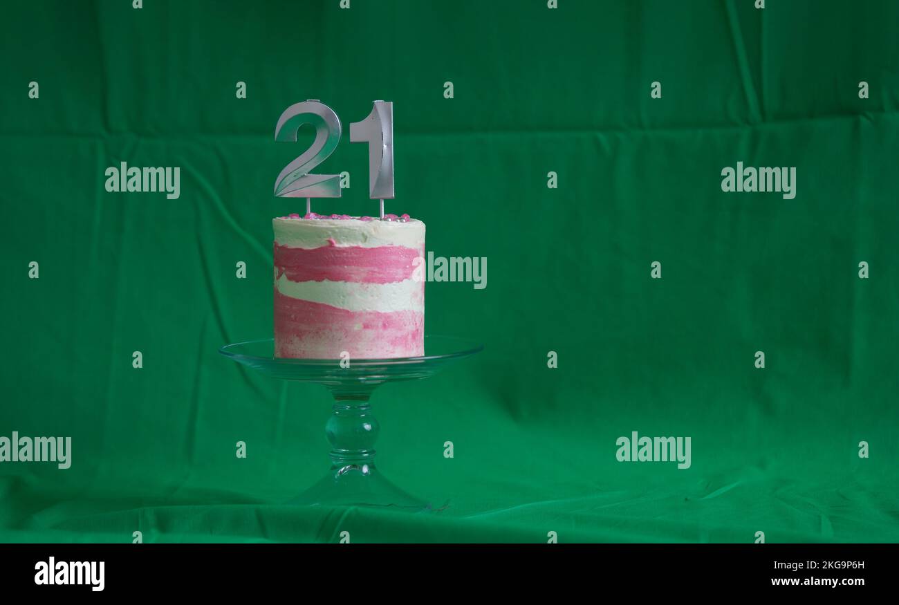 21st Birthday cake pink and silver cake with some sprinkles and 21st candlelight on a green background. Stock Photo