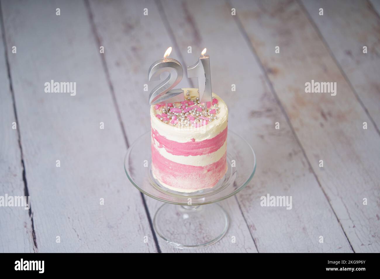 21st Birthday cake pink and silver cake with some sprinkles and 21st candlelight on a white wooden background. Stock Photo