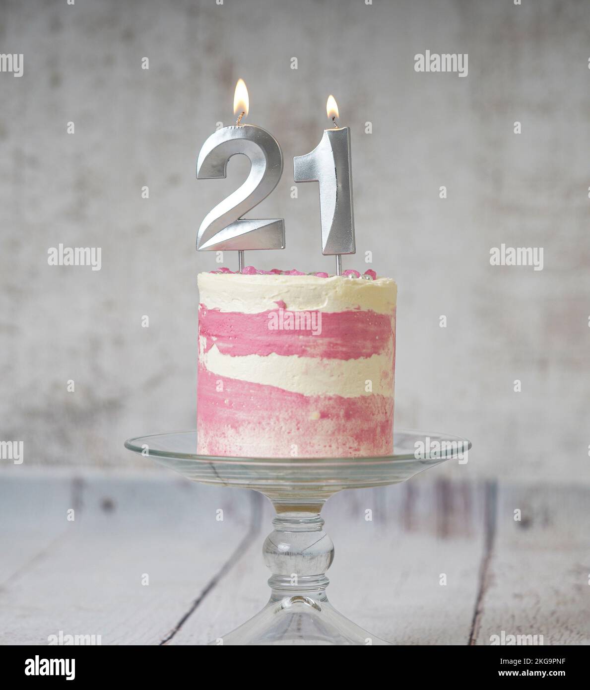 21st Birthday cake pink and silver cake with some sprinkles and 21st candlelight on a white wooden background. Stock Photo