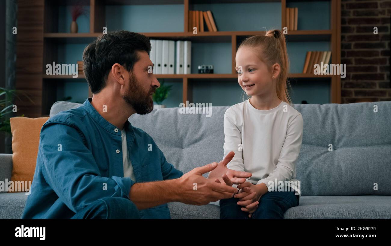 Caucasian man parent father psychologist talk to little cute kid girl teach small child of youth generation. Friendly dialogue with daughter at home Stock Photo