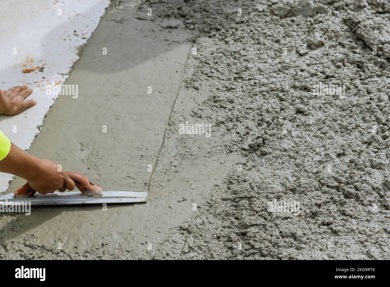 In construction area worker is holding steel trowel to smooth leveling over freshly poured concrete sidewalk Stock Photo