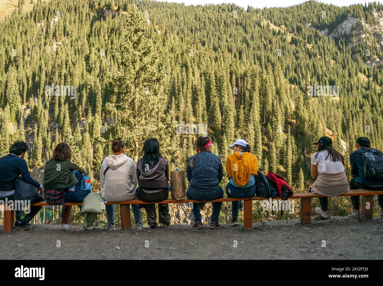 Kazakhstan tourism. Group of tourists sitting on the bench opposite to the thick forest of