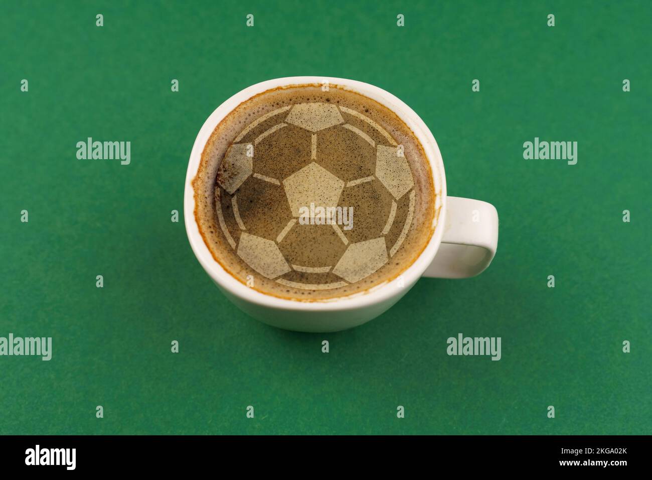 A cup of coffee with foam in the shape of a soccer ball. Cup on a green