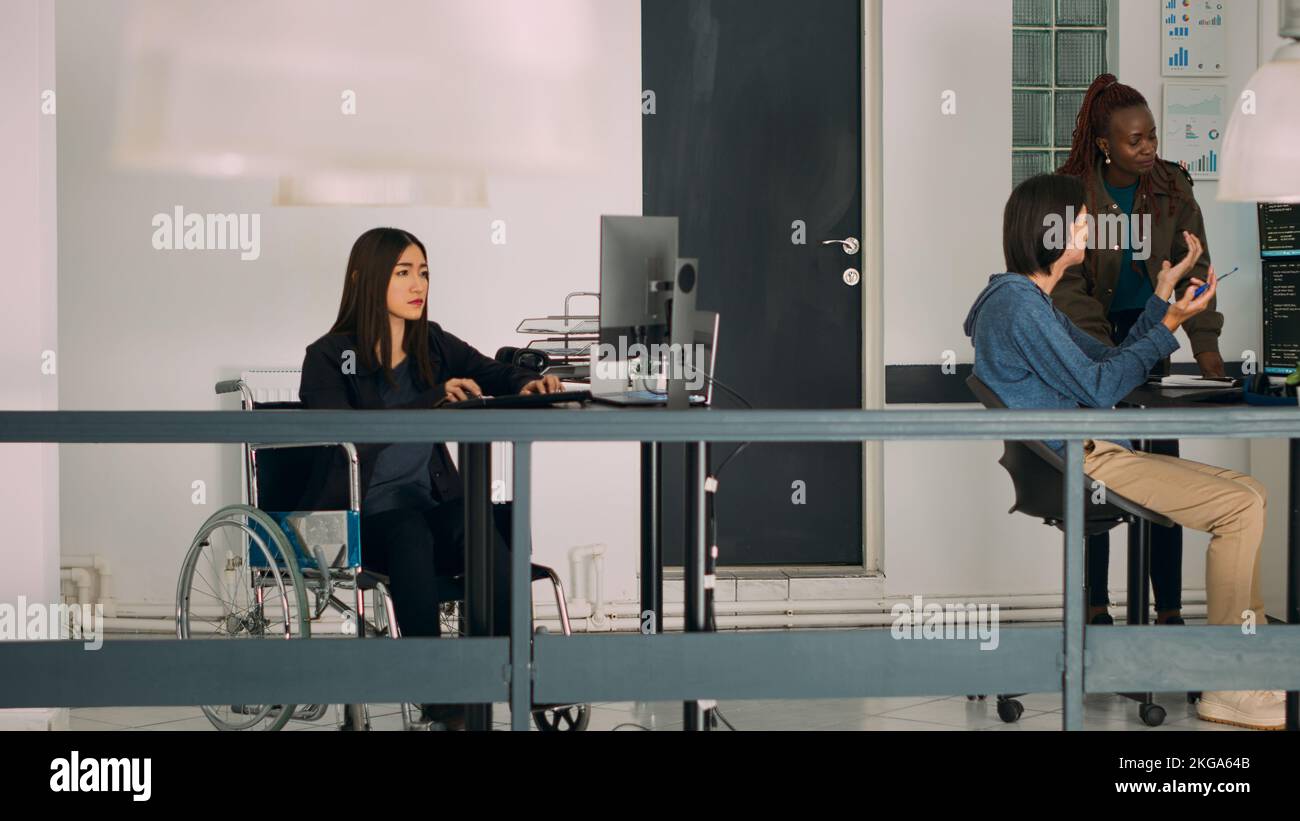 Asian system engineer with impairment programming app script on terminal window, using big data language. Developer in wheelchair working with cloud computing database, firewall security. Stock Photo