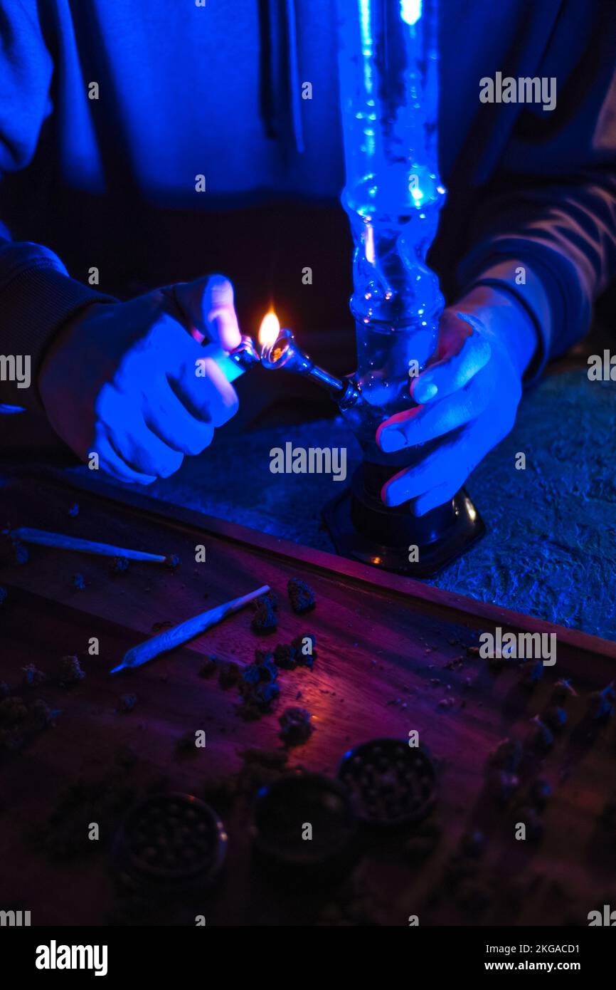 Male hands clog a bong with marijuana. A man smokes weed through a bong