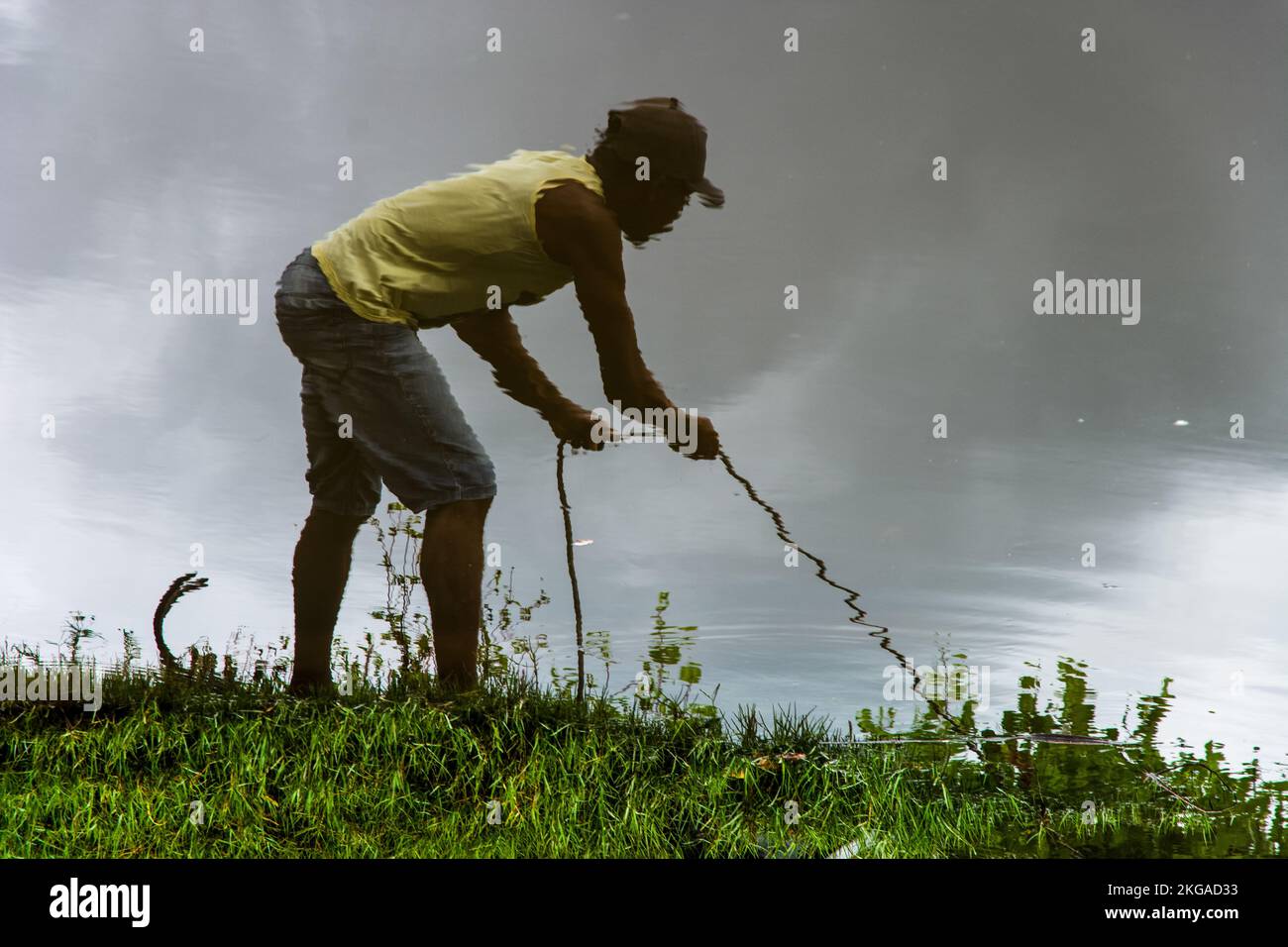 Reflection in the water of a man pulling a rope on the bank of the ...