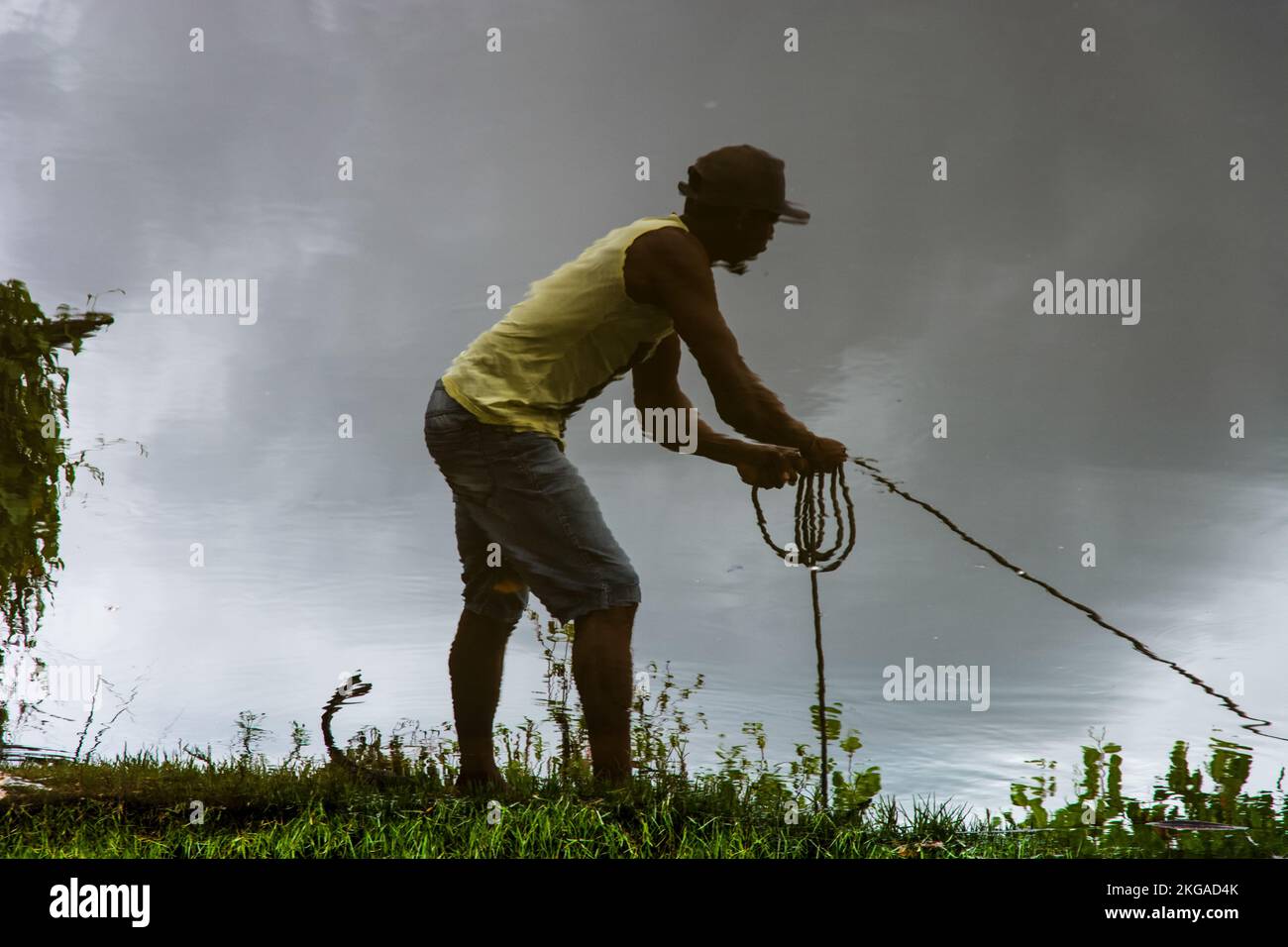 Reflection in the water of a man pulling a rope on the bank of the ...