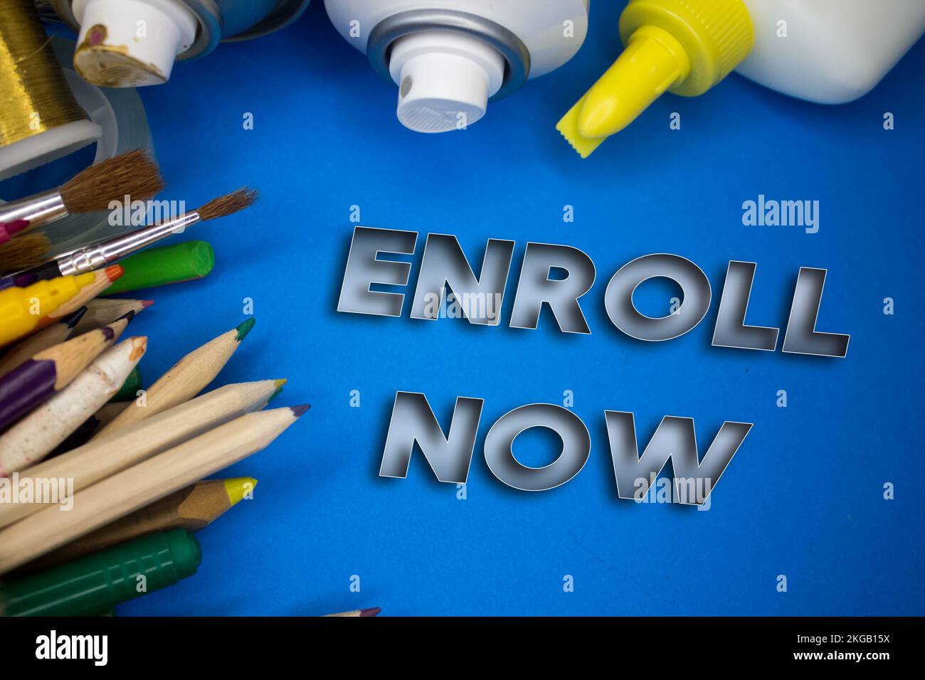 Overhead shot of school supplies with Enroll Now text. Brushes, pencils