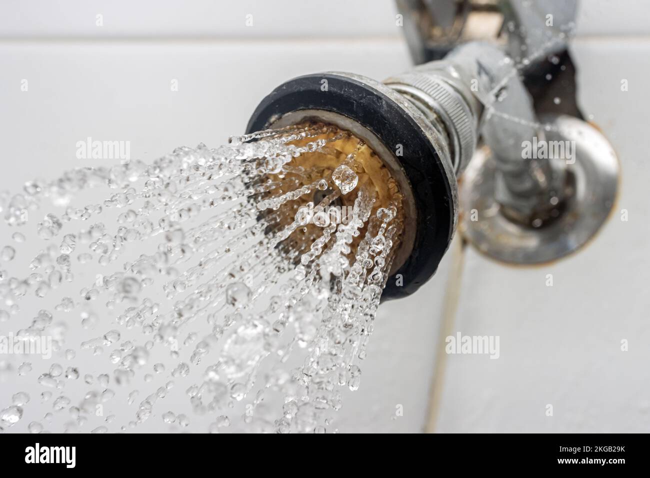 Water flows from an old shower head fixed in the bathroom wall Stock