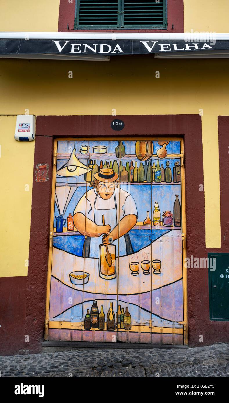 Colourfully painted door with bartender preparing poncha, art project Arte de portas abertas, Rua de Santa Maria, Old Town, Funchal Madeira, Portugal, Stock Photo