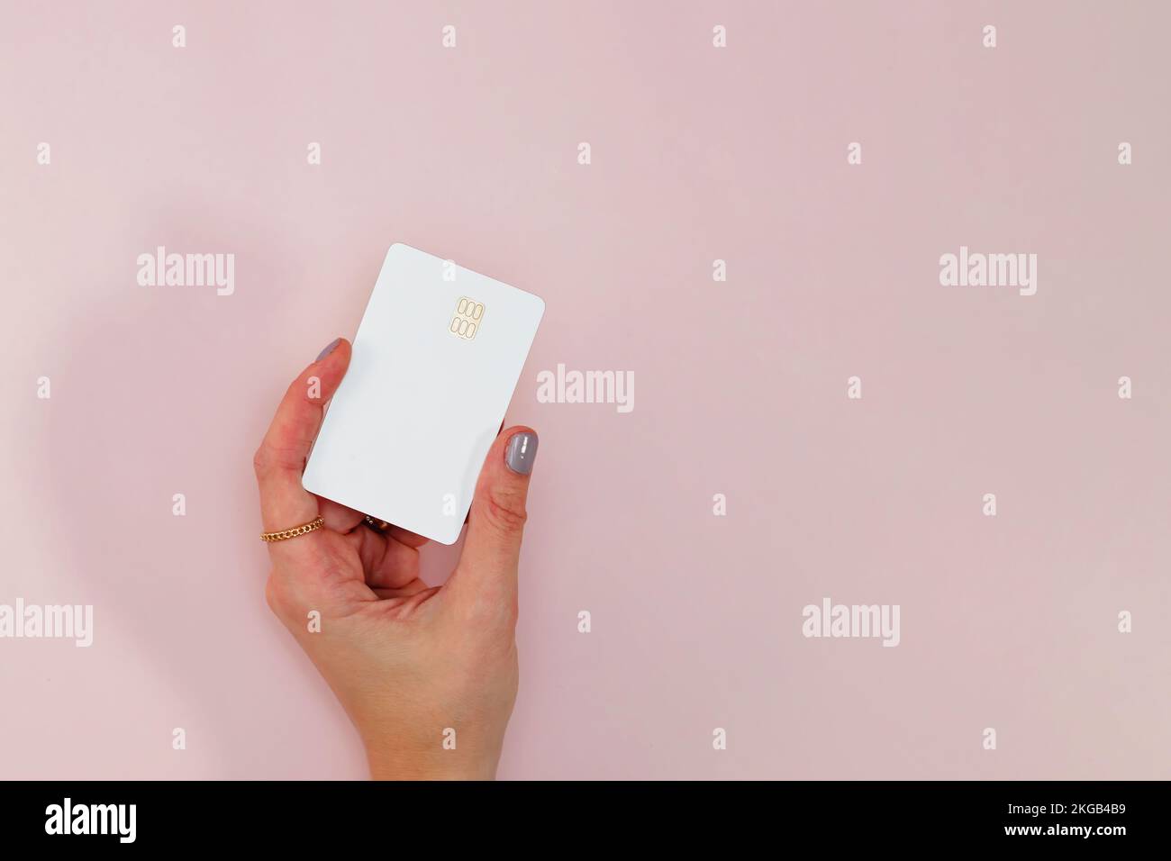 Woman's hand holding white plastic credit or debit card with chip over the pink background Stock Photo