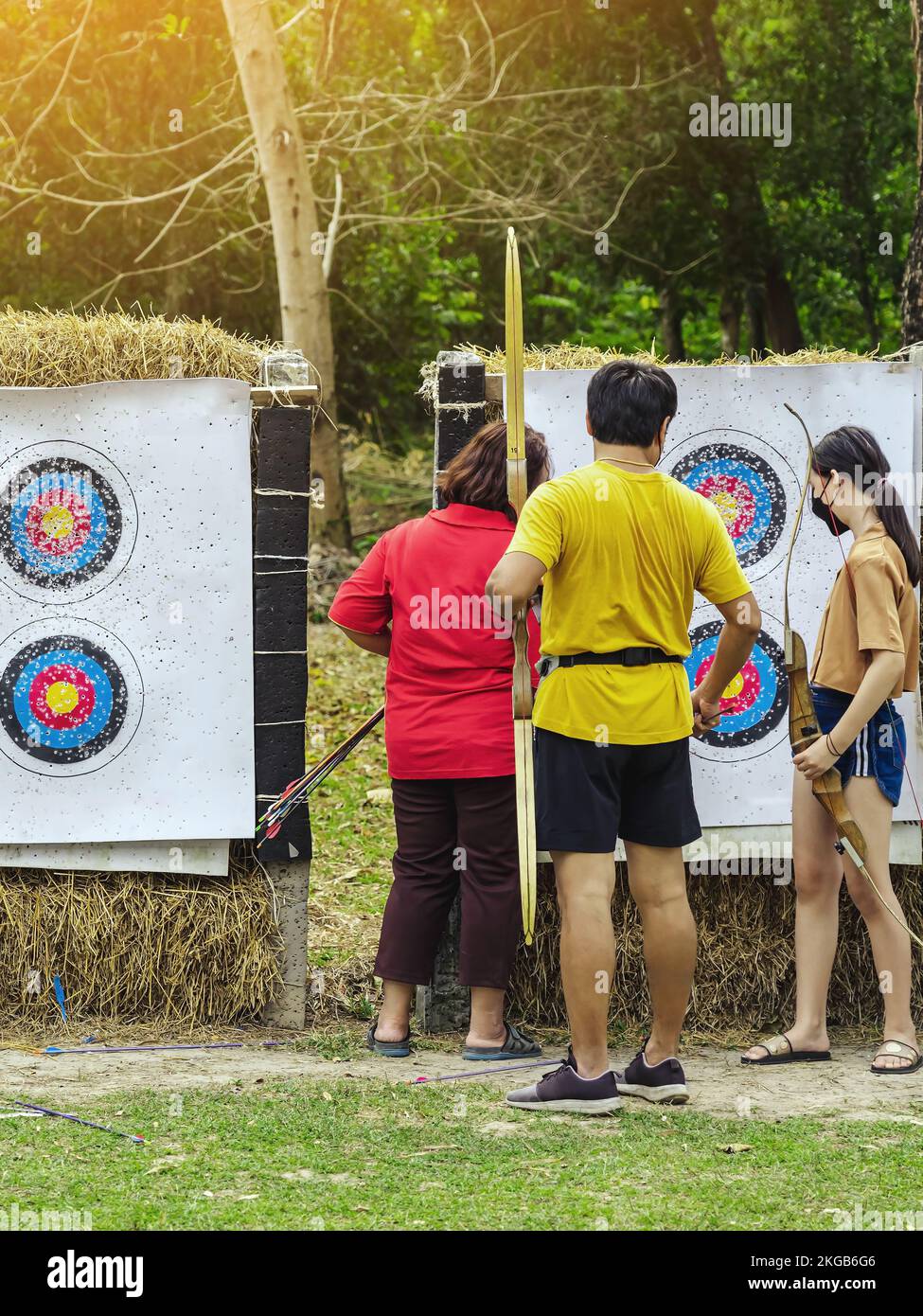 Back view of Asian archers wear face mask collect arrows fired from a bow on sport target. Archer clearing arrows from target to start new game. Medit Stock Photo