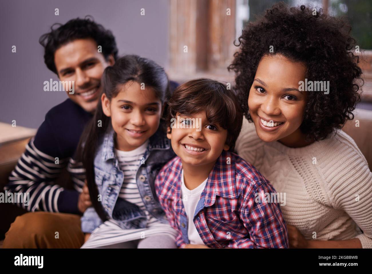 They complete each other. Portrait of a happy family of four sitting together on a sofa at home. Stock Photo