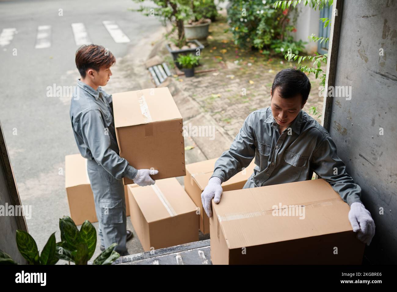 Movers in grey uniform loading cardboard boxes with belongings on ...