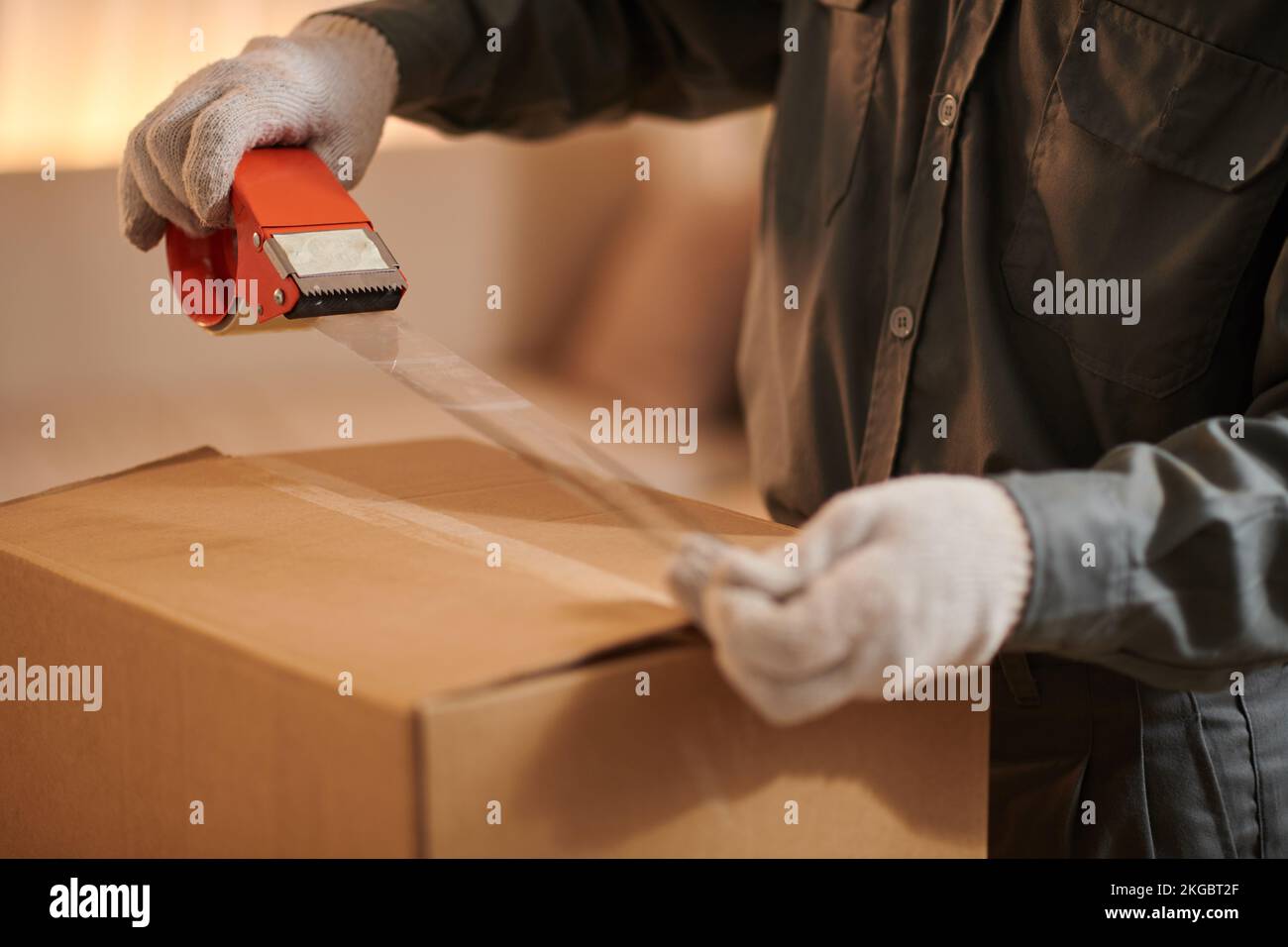 Closeup image of mover sealing shipping cardboard box with adhesive