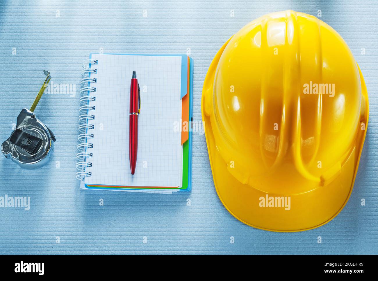 Checked notebook pen hard hat tape measure. Stock Photo