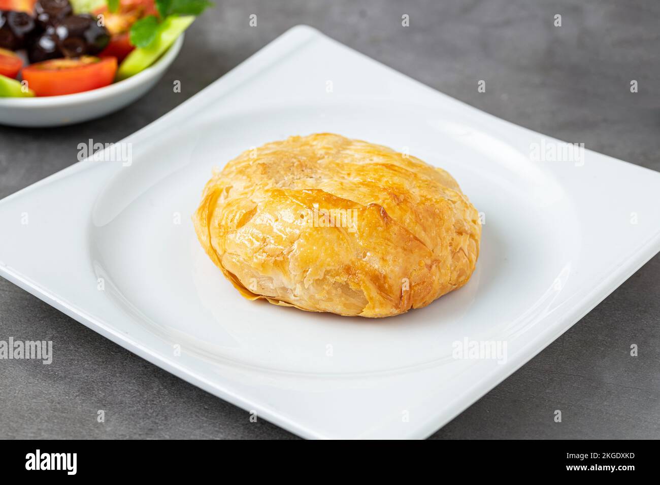 Turkish boyoz with olives, cucumbers and tomatoes next to it on a dark stone table Stock Photo