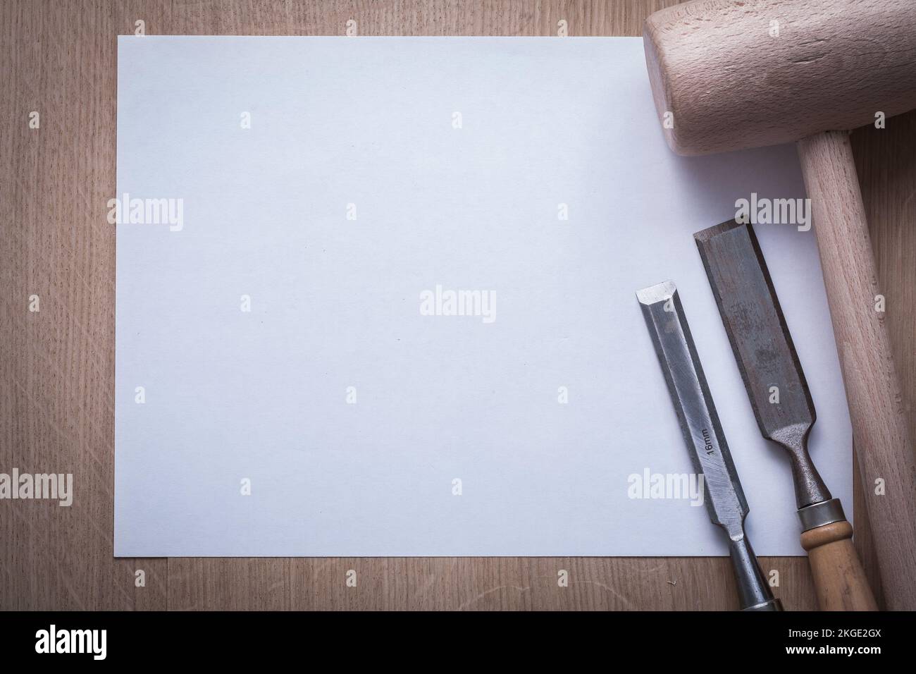 Firmer chisels lump hammer and clean sheet of paper on wooden board copy space construction concept. Stock Photo