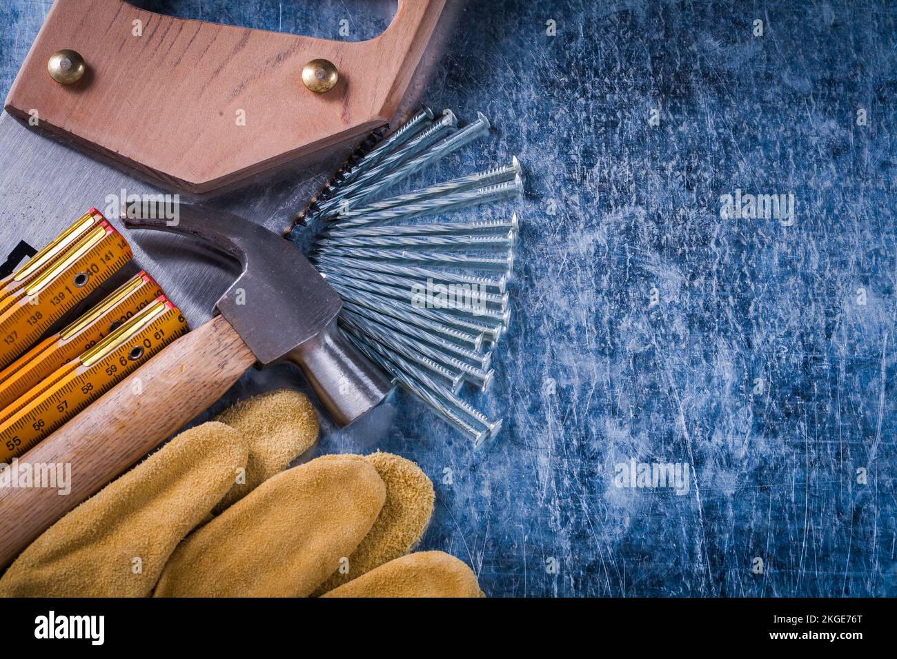 Hand saw safety gloves construction nails wooden meter and claw hammer on scratched metallic